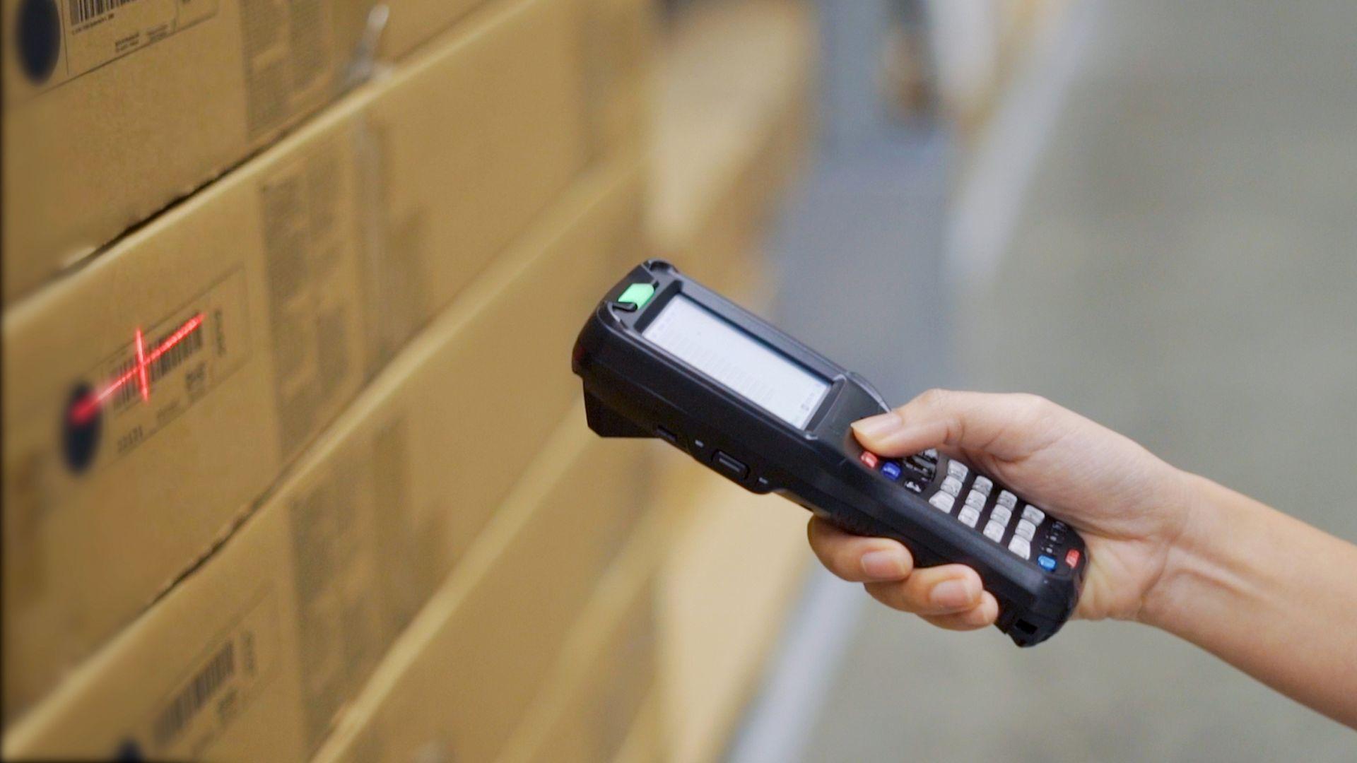 Nahaufnahme eines mobilen Barcodescanners beim Scannen von Kartonetiketten im Logistikbereich