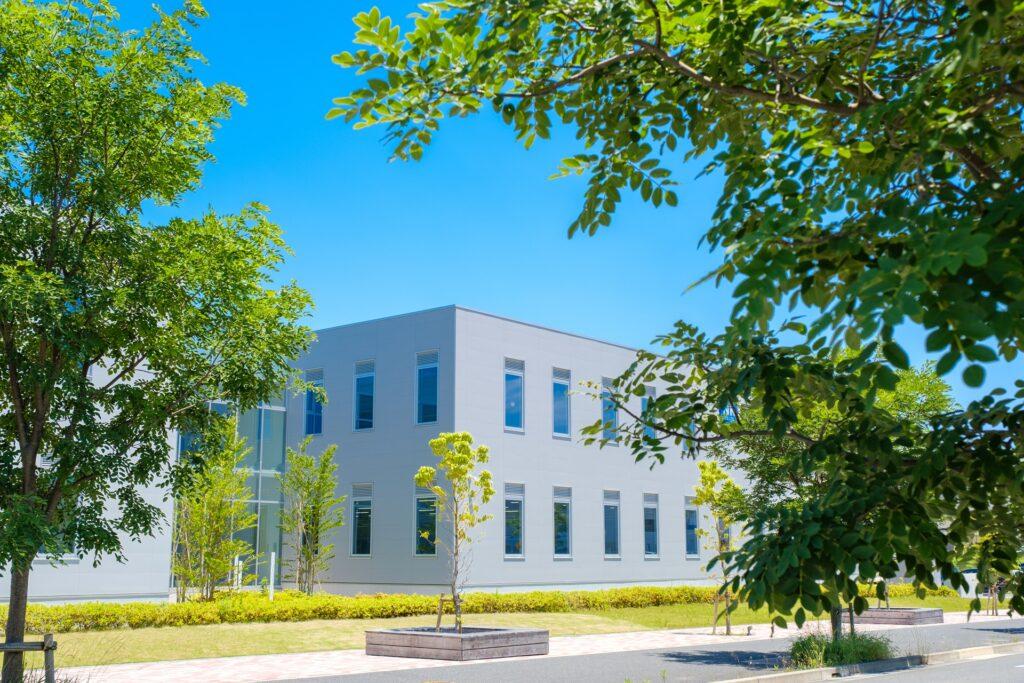 Modernes hellgraues Bürohaus umgeben von grüner Gartenanlage | Mülltonnenbox